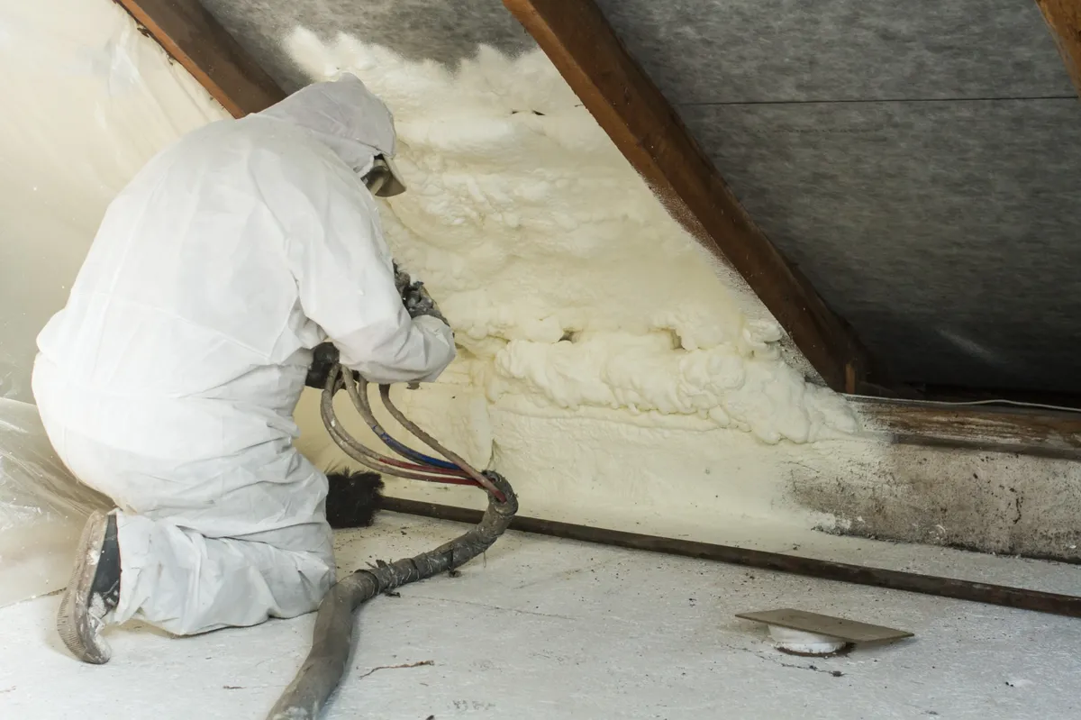 Technicien appliquant de la mousse isolante sous la charpente pour l'isolation des combles.